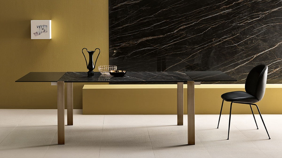 Dining table with a black veined Laminam top in front of a full-height Laminam slab wall, with an ochre wall and black leather chair