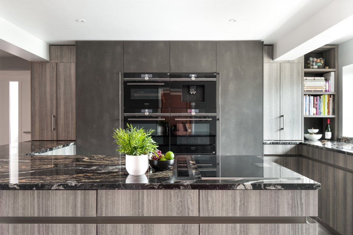 Kitchen island with a polished dark Sensa granite top in front of grey tall units with built-in ovens